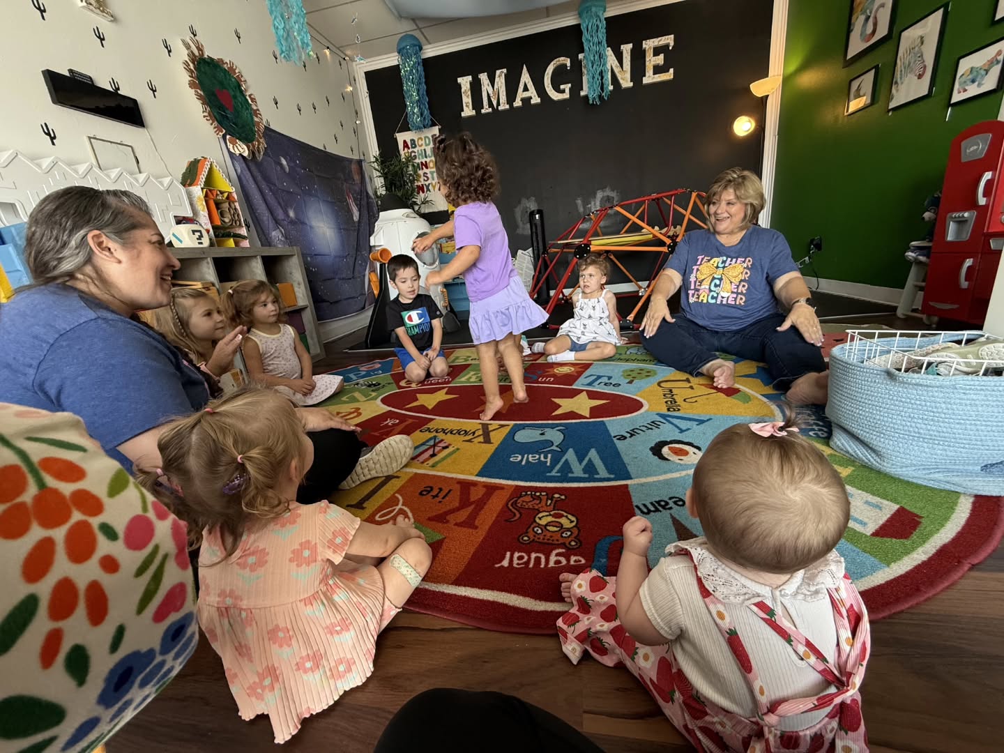 Kids and grown-ups sitting in a circle on the alphabet rug with their teachers